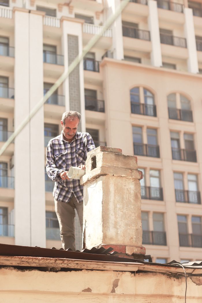 Crafting Captivating Headlines: Your awesome post title goes here Man in plaid shirt repairing chimney on a city rooftop with modern buildings in background.