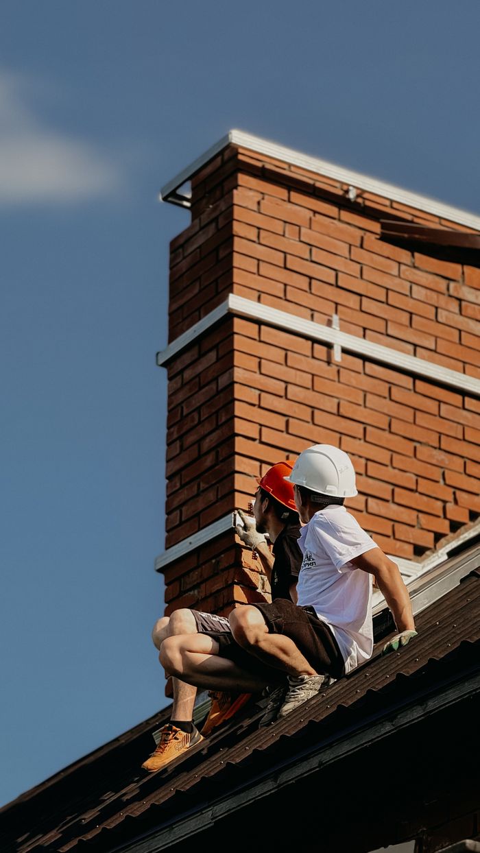 The Art of Drawing Readers In: Your attractive post title goes here Two construction workers with hard hats repairing a chimney on a house roof under a clear sky.